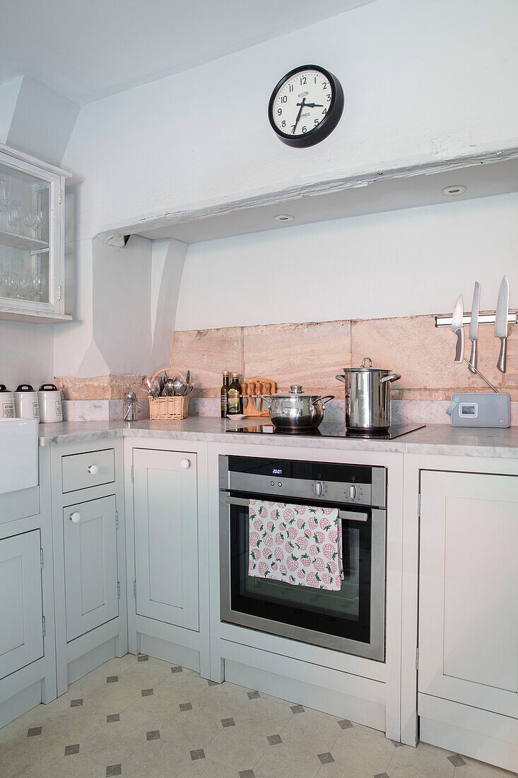 Clock above oven with pans on hob and walls in Pavilion Grey in Wiltshire kitchen UK