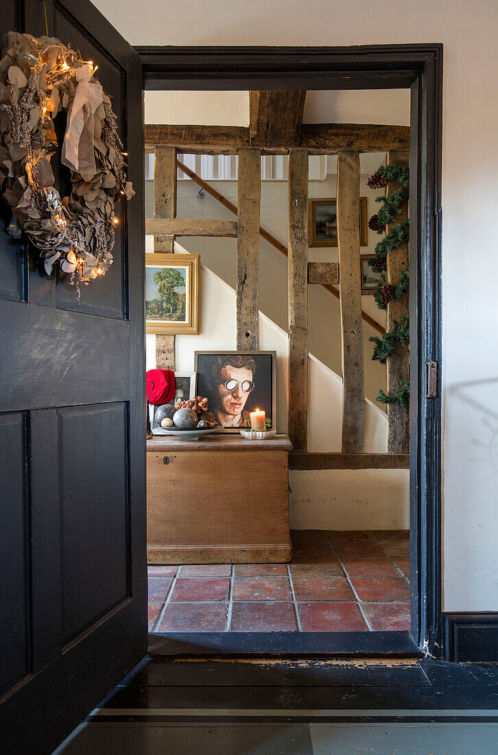 Tür in Off Black mit Weihnachtskranz und Terrakottafliesen im Fachwerkflur eines Bauernhauses in Norfolk, Großbritannien
