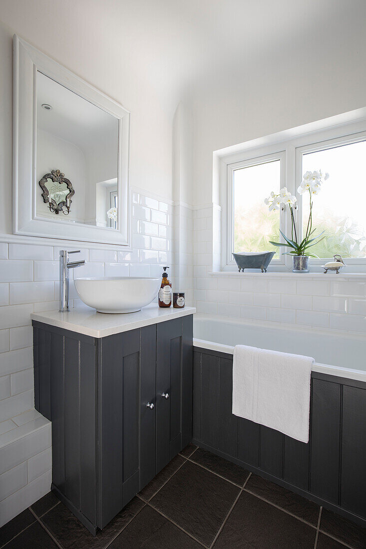 Grau getäfelte Badewanne und Waschtisch mit Orchidee auf der Fensterbank in einem Landhaus in Surrey, UK