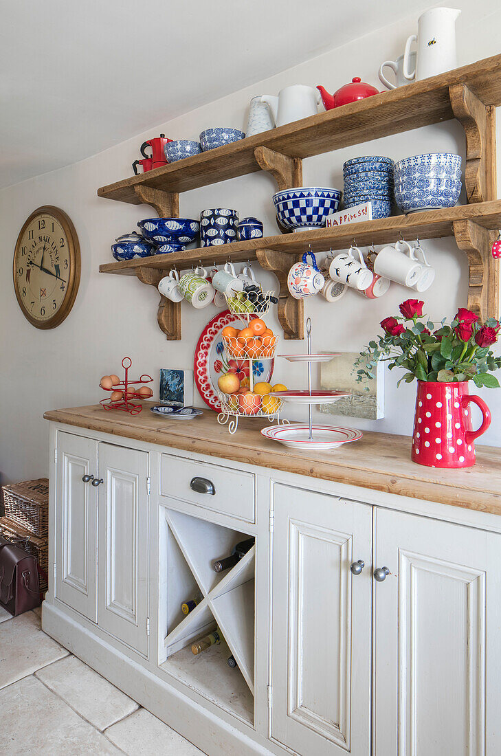 Verschiedene Tassen und Schalen auf Holzregalen über einer freistehenden Kommode in einem viktorianischen Cottage in Pavilion Grey, Midhurst, West Sussex, Großbritannien