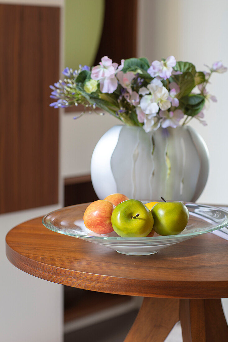 Vase of flowers and bowl of apples on tabletop London UK