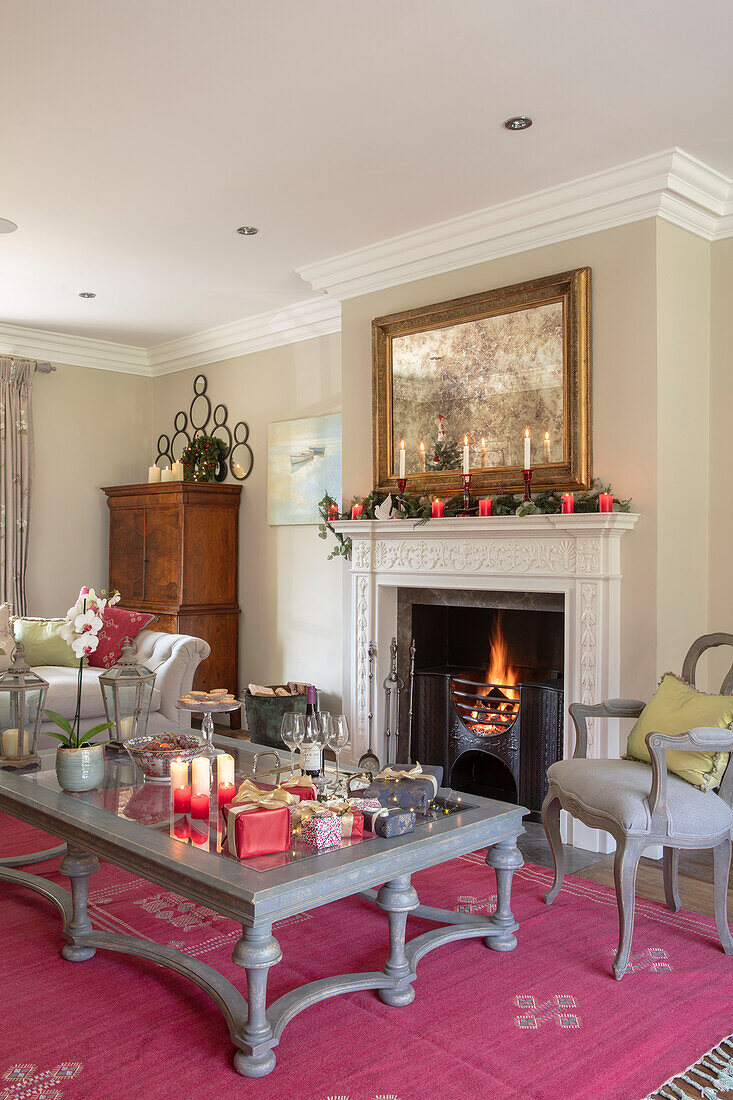 Spiegel über dem beleuchteten Feuer mit grauem Couchtisch und Stuhl und Cayuga-Teppich an den Wänden in einem Landhaus in Portland Stone Hampshire UK