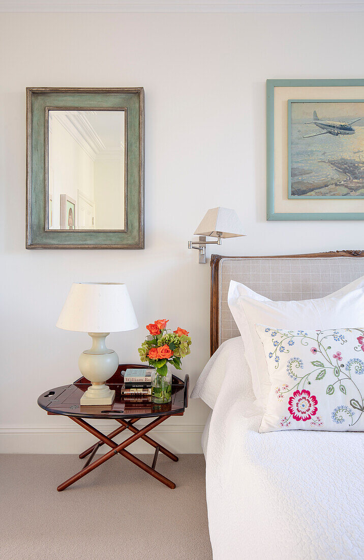 Lamp and cut flowers with mirror at bedside in Southwest London home UK