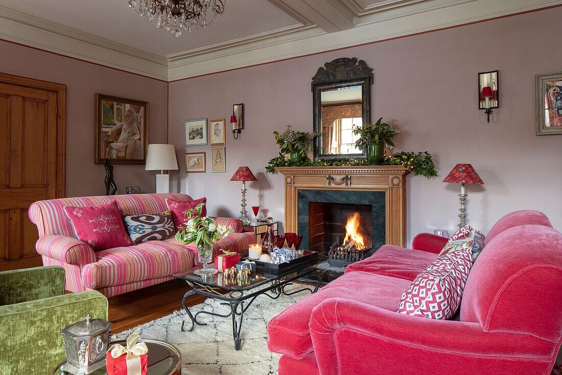 Pinkfarbene Sofas und beleuchtetes Feuer in einem unter Denkmalschutz stehenden georgianischen Landhaus in West Sussex, England