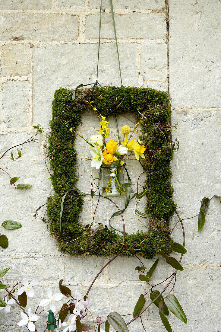 Glas mit gelben Blumen in einem Moos-Bilderrahmen auf einem Stein im Freien, Isle of Wight, UK