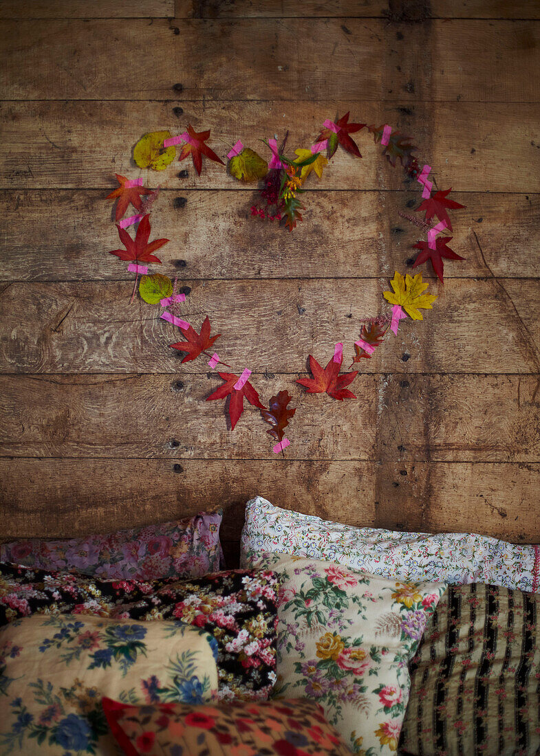 Heart of leaves above assorted floral cushions in rustic wood cabin Autumn UK