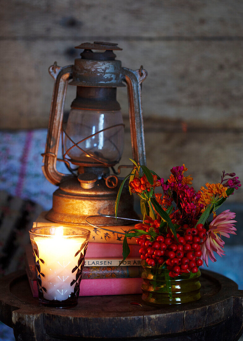 Lit candle and cut flowers with hurricane lamp on books in Autumn UK