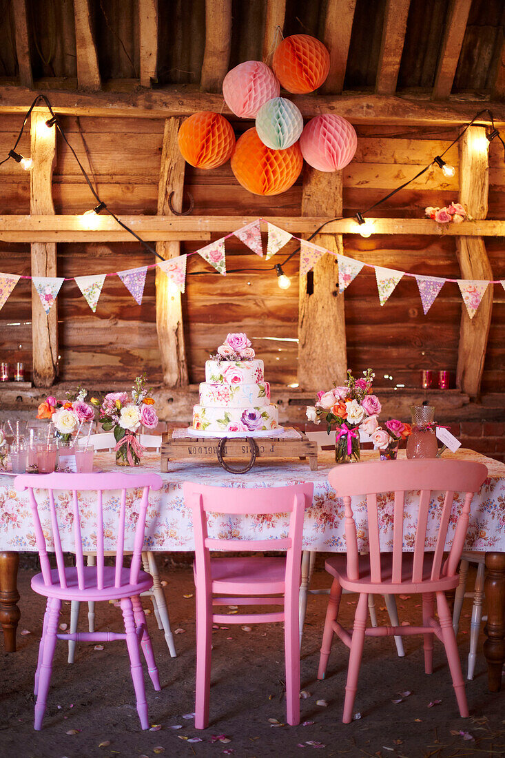 Pinkfarbene Stühle und Stufenkuchen mit Wimpeln und Lichtern in einer Holzhütte im Spätsommer UK
