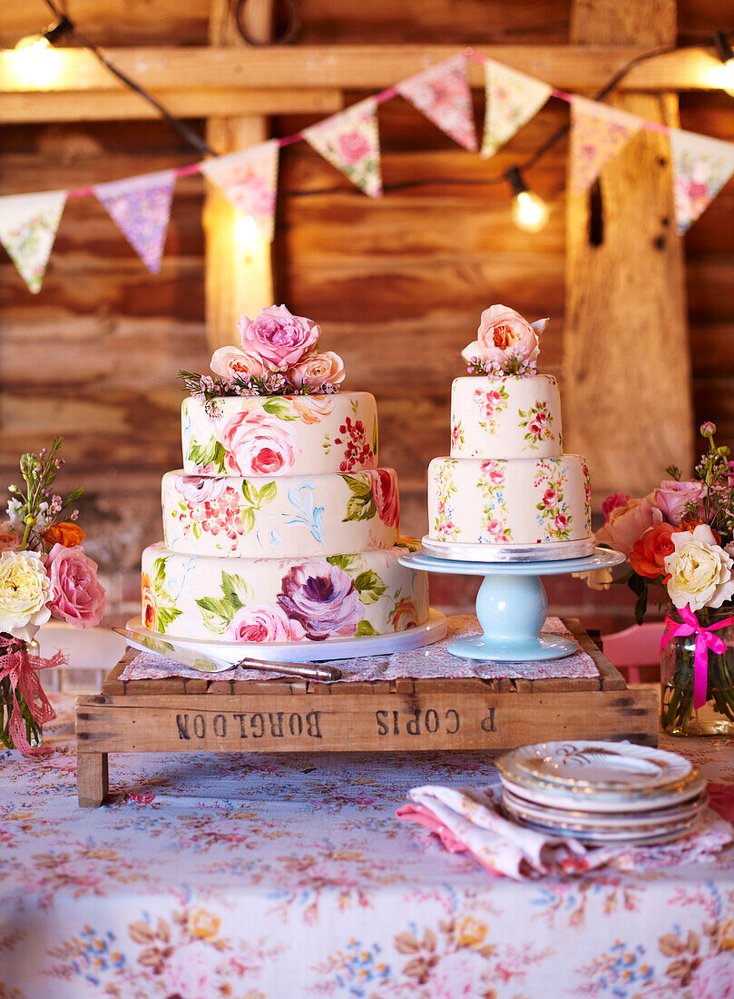 Iced cakes and sideplates with bunting and lights in wooden barn late summer UK