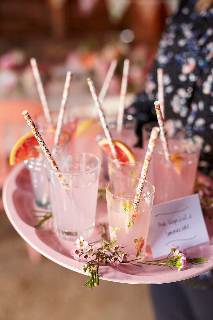 Frau trägt Tablett mit rosa Grapefruitlimonade in Gläsern mit Strohhalmen