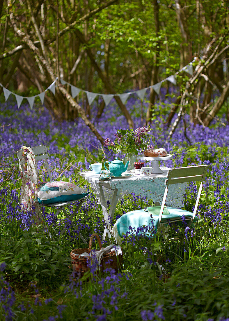 Table and chairs set for picnic with bunting in bluebell woods