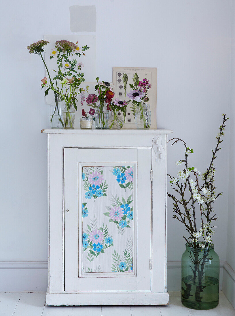 Weißer Schrank mit Blumentapeteneinsatz mit botanischen Drucken und frischen Blumen in Glasvasen