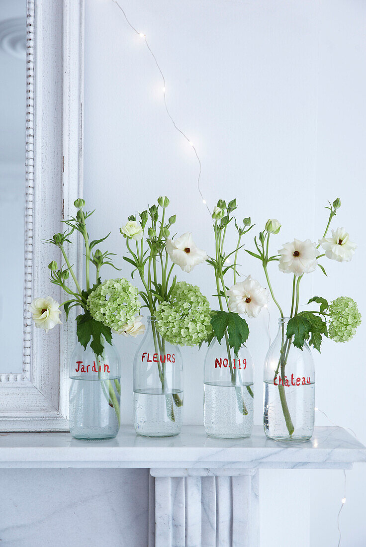White marble Mantelpiece and mirror detail with four glass milk bottles with red writing on displaying fresh cut flowers and fairylights