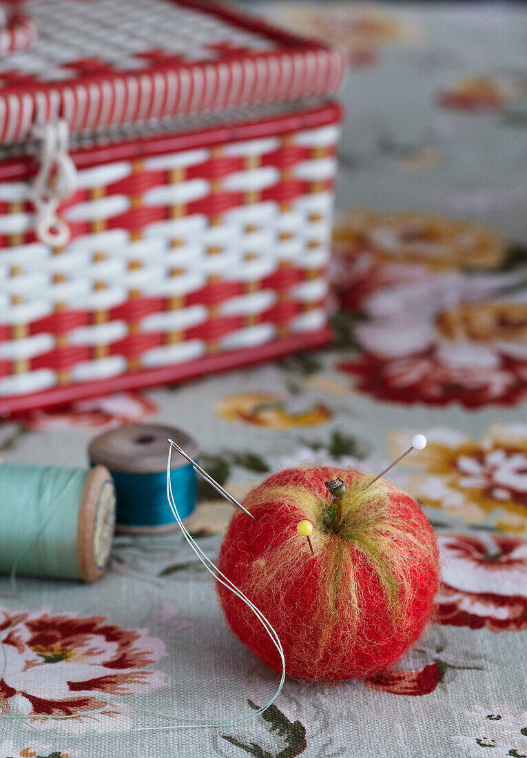 Needle felt apple with pins beside a Vintage sewing box