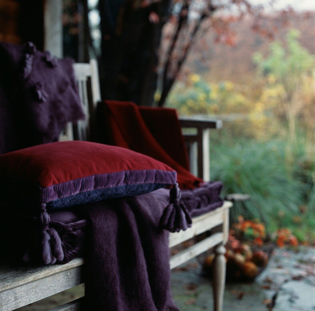Wooden garden bench with blanket and cushions in a garden out house on an autumnal day