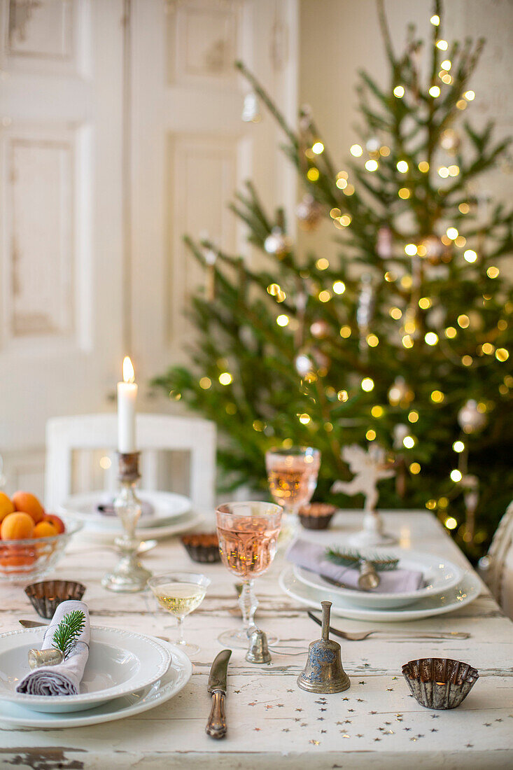 Festive table setting in dining room with decorated Christmas tree and lit candles