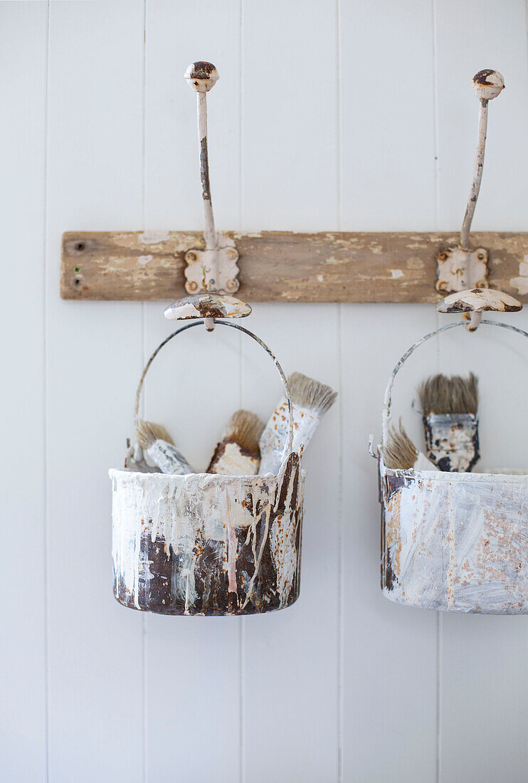 Detail of vintage paint pots with brushes hanging from coat hooks