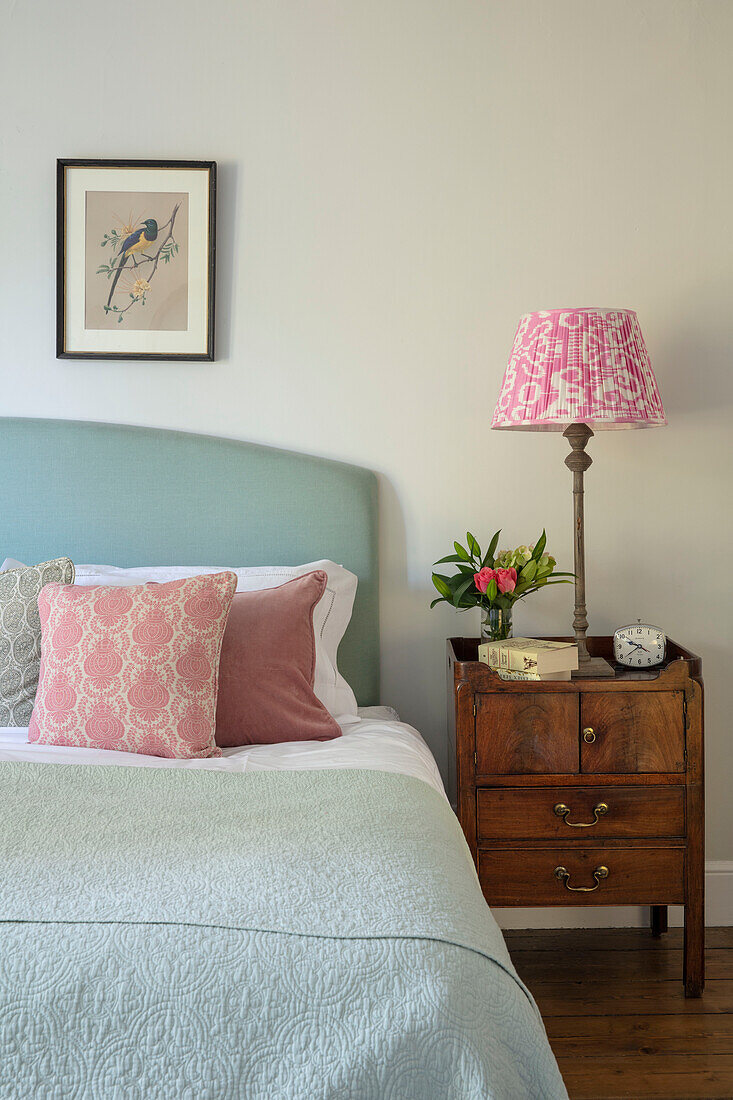 Bed with throw pillows and antique bedside table with lamp