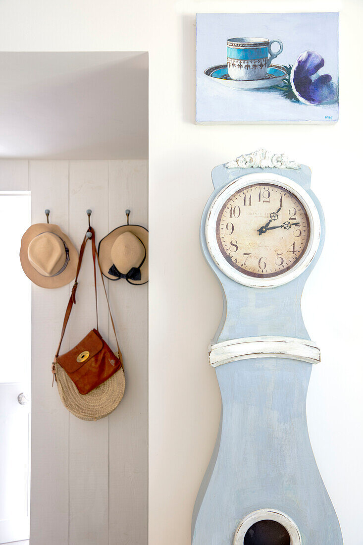 Wall with grandfather clock and painting, coat hooks with hats and bags in the background