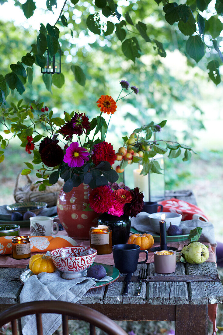 Gedeckter Tisch im Garten mit Herbstdeko, Blumenarrangement und Kürbissen