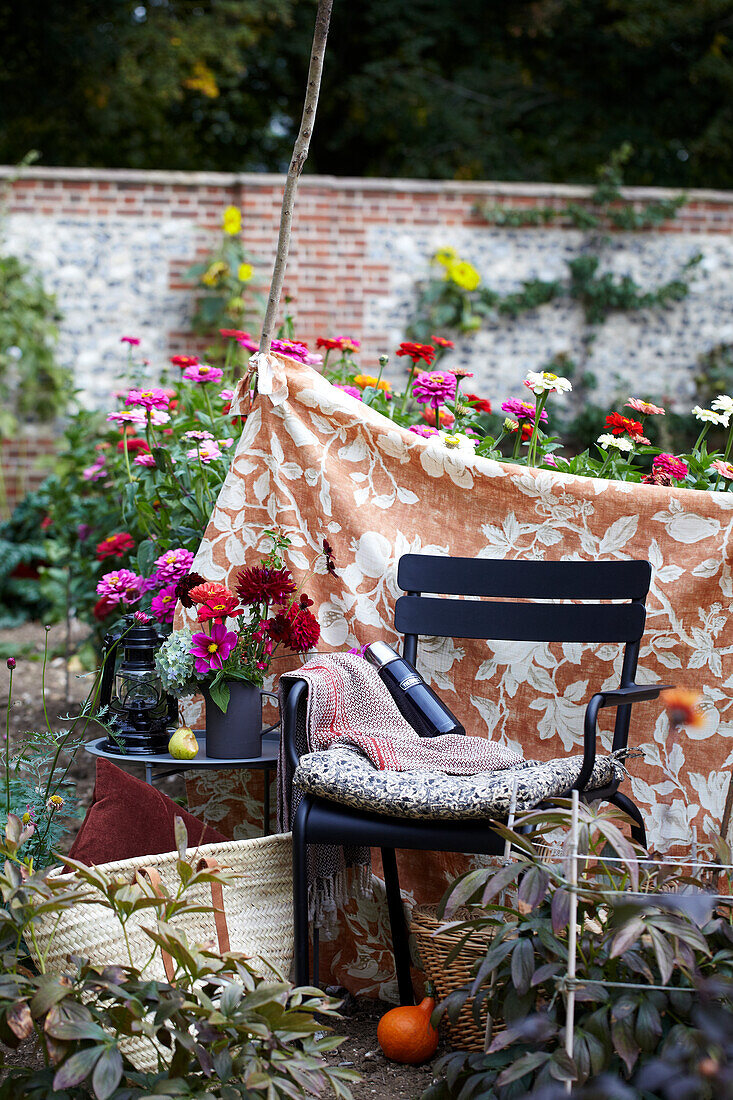 Kleine Ecke im Garten mit Blumen, Stuhl und gemusterter Decke als Abtrennung