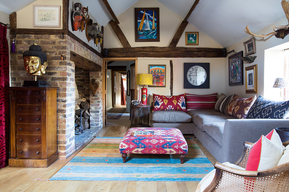 Sofa and ottoman in front of open brick fireplace, artwork on wall in living room