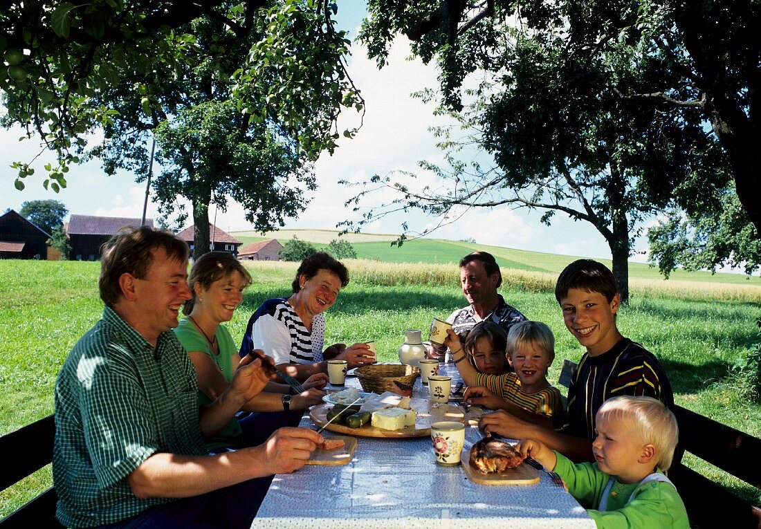 Familie bei der Bretteljause (Brotzeit) unter Bäumen am Feld