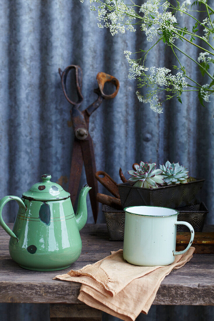 Green teapot, cup and succulents in a baking tin on a wooden table