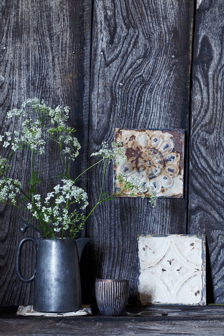 Metallkanne mit Wildblumen vor rustikaler Holzwand