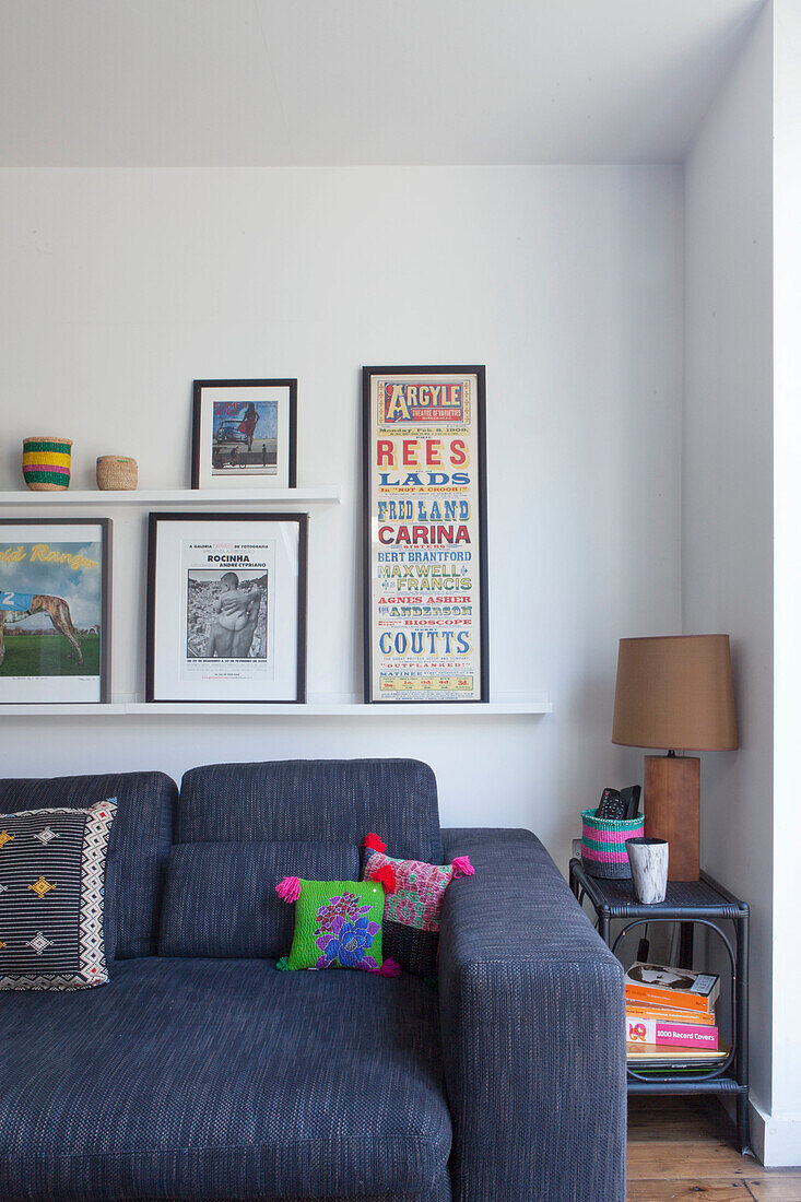 Blue sofa with scatter cushions and side table below collection of pictures on shelves