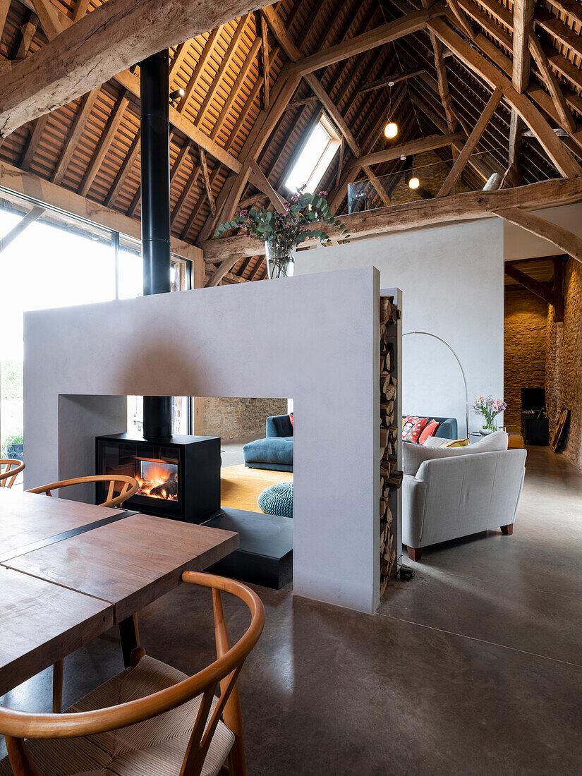 View of living room area with large double sided fireplace and large dining table in a former barn