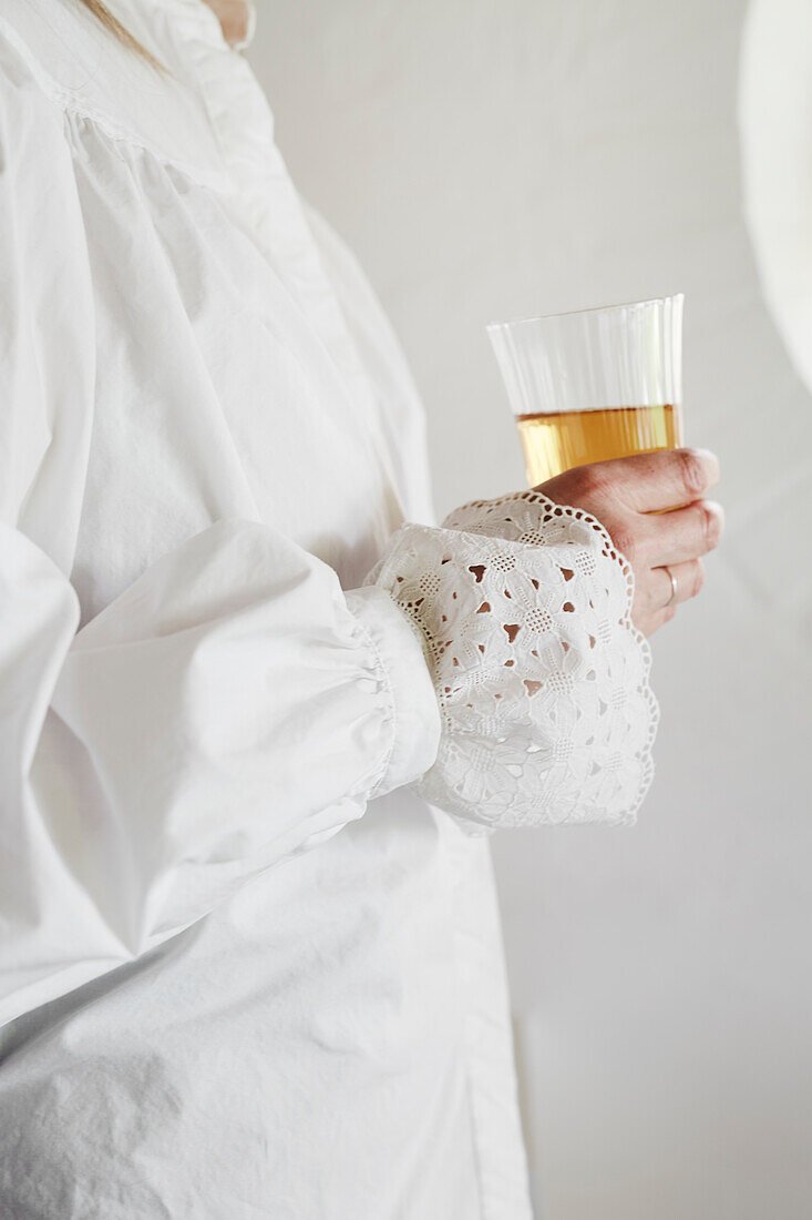 Woman in white blouse with lace sleeves holds a glass in her hand