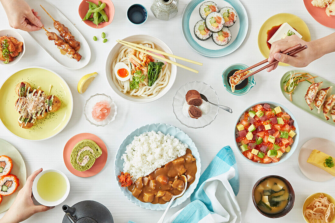 Elegantly laid table full of Japanese dishes with peoples hands (filling the frame)