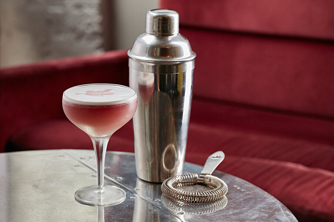 Rosa Cocktail in einem Martini-Glas dahinter Cocktailshaker