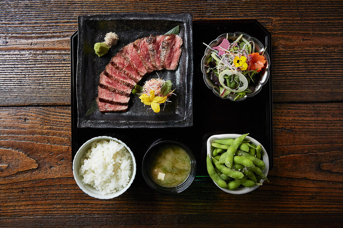 Delicately presented Japanese lunch dishes, Beef, rice, miso soup, edemame and salad.