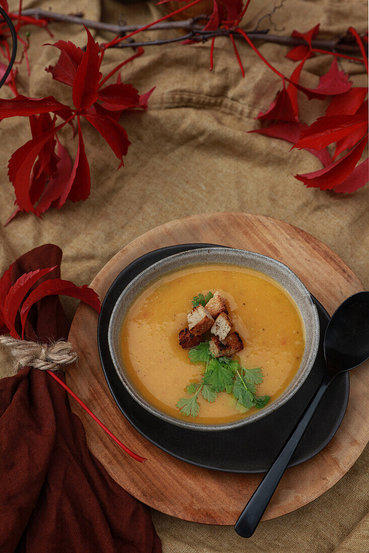 Kürbissuppe mit Koriander und Croutons auf herbstlich gedecktem Tisch