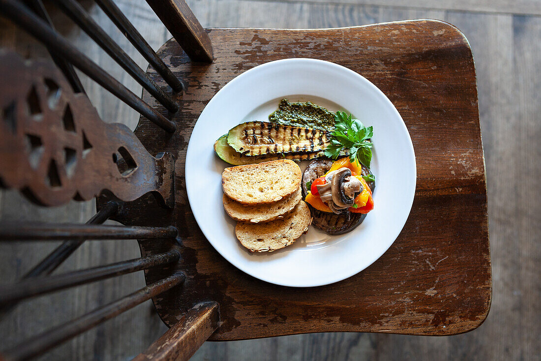 Grilled vegetables (aubergines, courgettes, mushrooms, peppers) with pesto and soda bread on a wooden stool