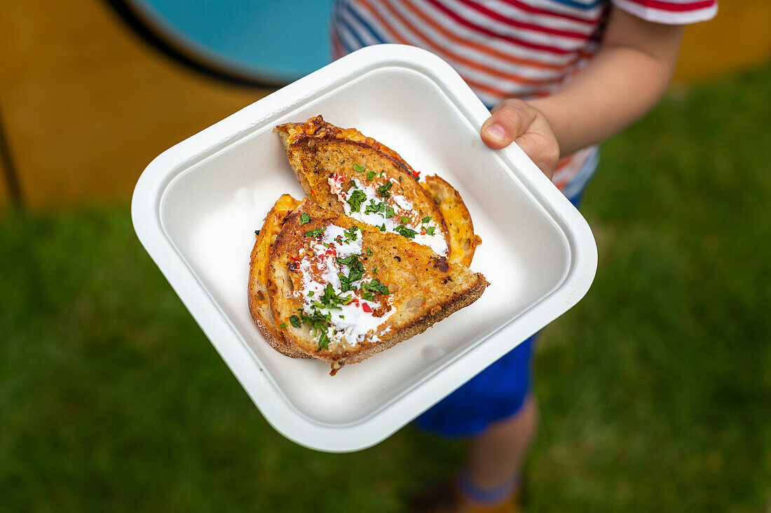 Child holding cheese toast with chilli jam, sour cream and coriander