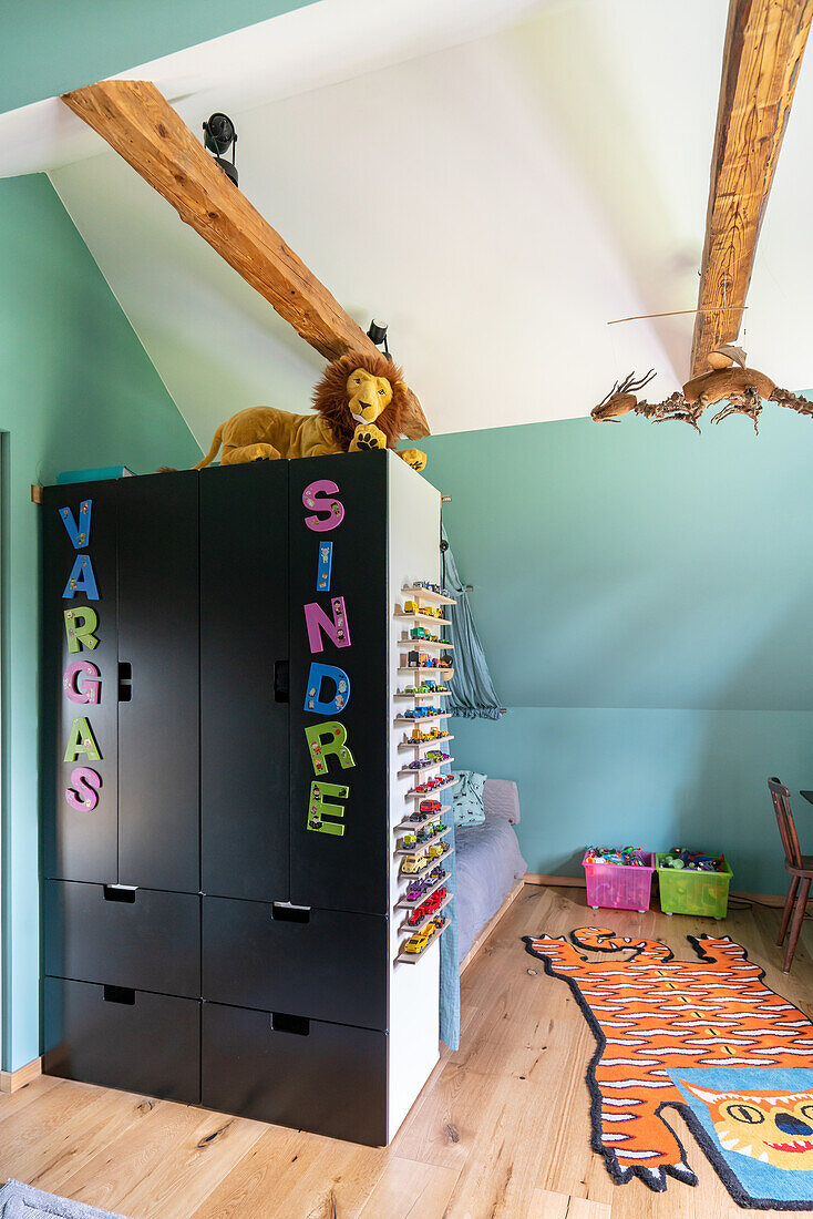 Kinderzimmer mit Dachschräge, schwarzem Schrank, buntem Teppich und Spielzeugaufbewahrung