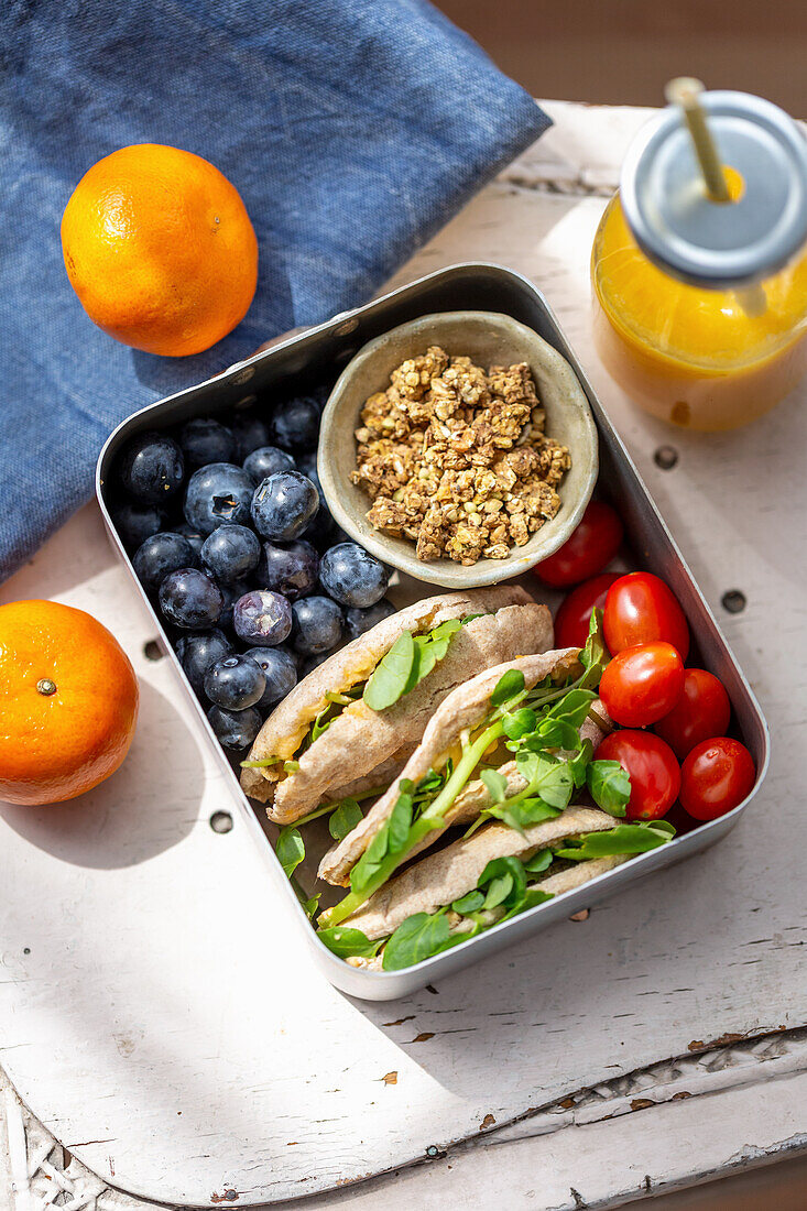 Lunchbox mit gefülltes Pitabrot, Granola, Tomaten und Blaubeeren