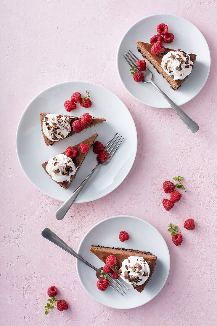 Schoko-Käsekuchen mit Keksboden, garniert mit Sahne, Himbeeren und Schokoraspeln