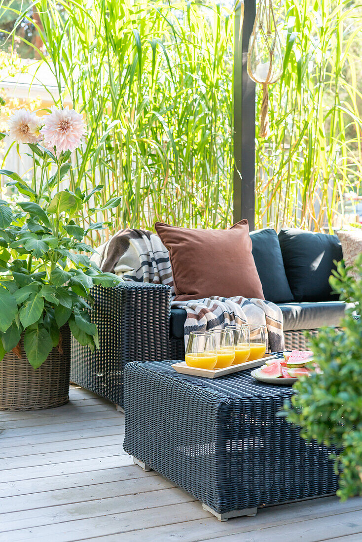 Rattan-Sitzgruppe auf Terrasse mit Kissen, Decke und Orangensaft