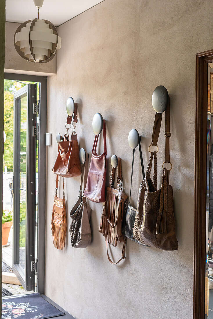 Lederhandtaschen an Wandhaken im Eingangsbereich mit Pendelleuchte