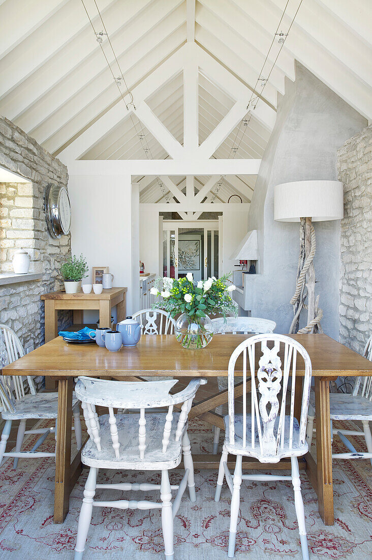 Bright dining area with wooden table, various chairs and stone wall