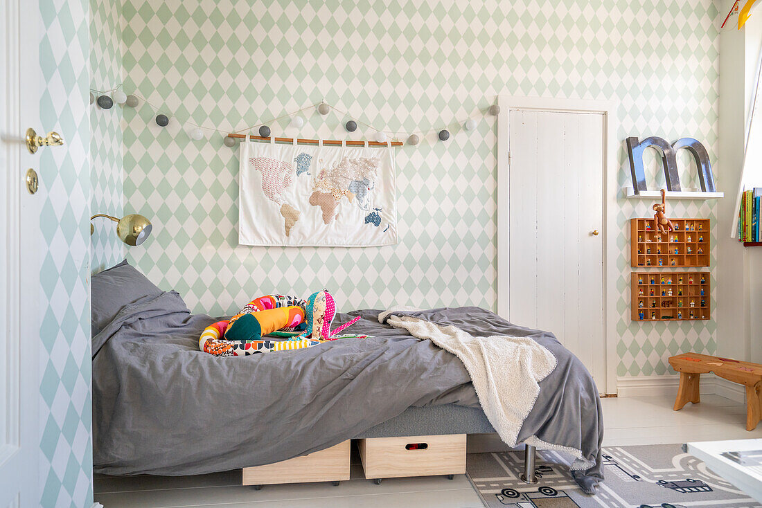 Wallpaper with diamond pattern, bed with colourful cuddly snake and play rug in children's room