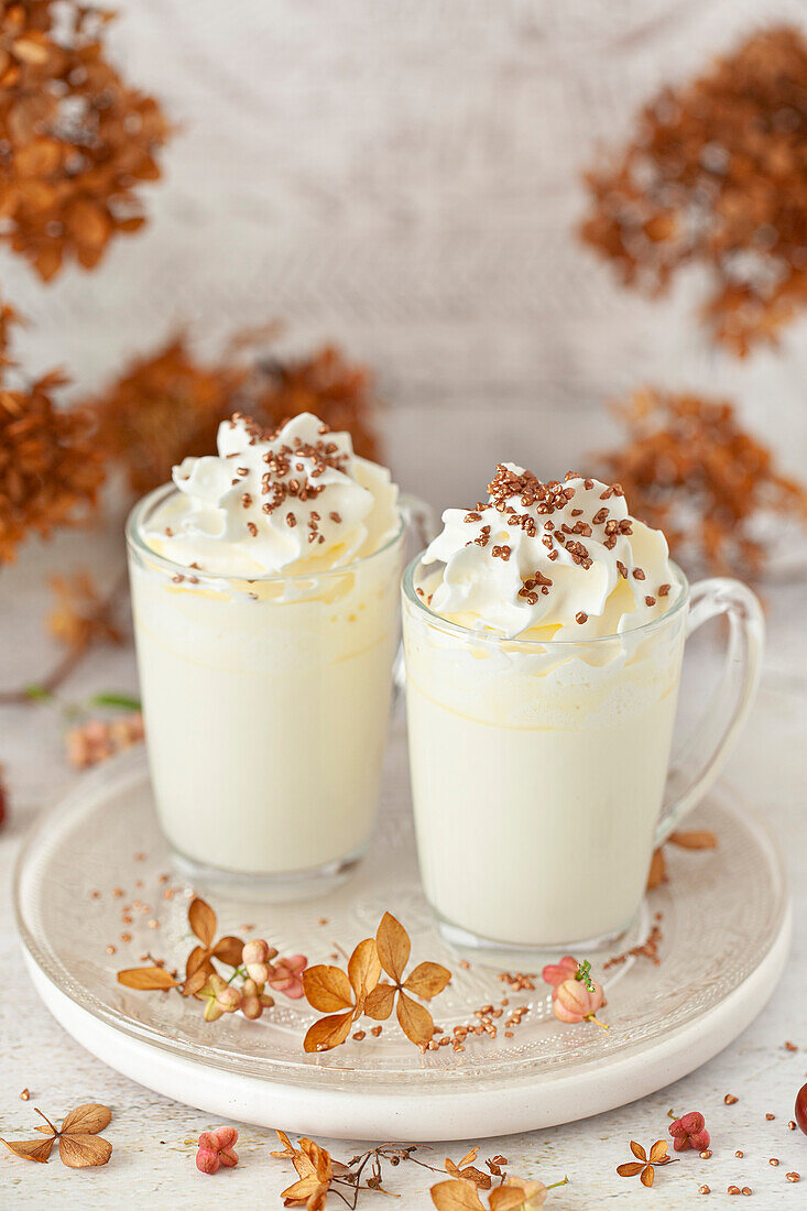 Two glasses of white hot chocolate with cream and bronze sprinkles