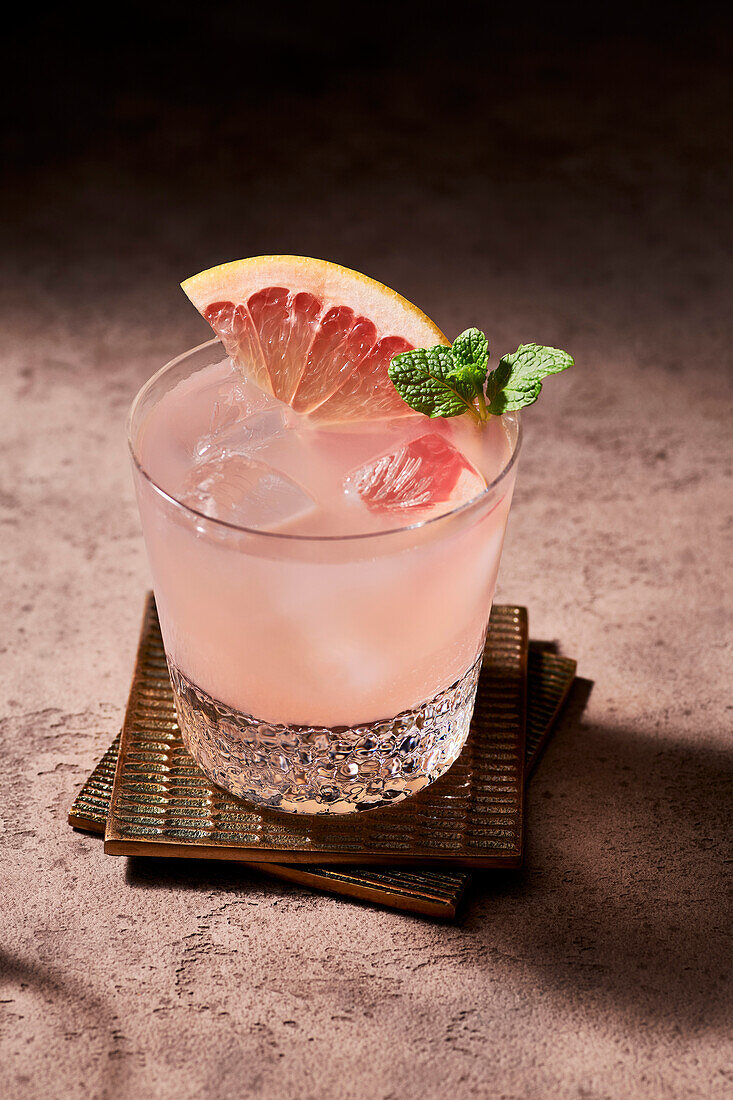 Paloma cocktail garnished with a grapefruit slice and mint sprig on two copper coasters