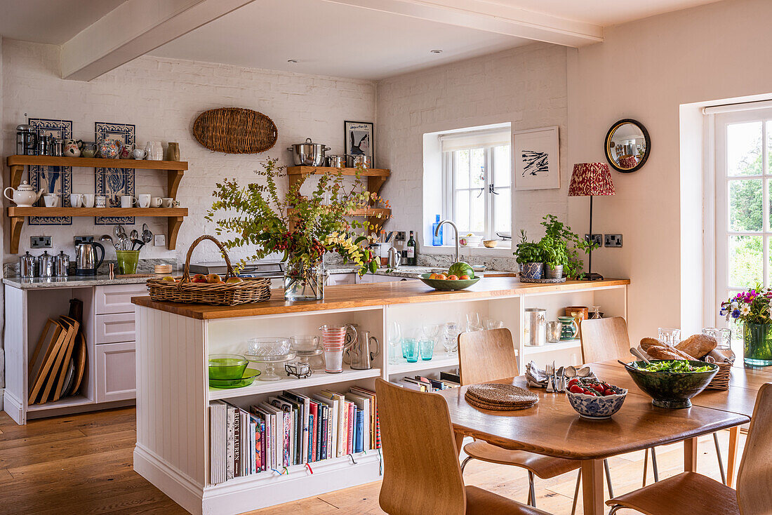 Landhausküche mit Holztisch, offenen Regalen und Dekoration aus Blumen in einer Vase