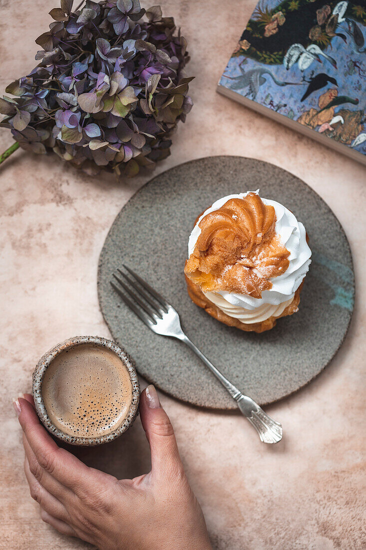 Woman drinking coffee and eating cream puff dessert served on a ceramic dessert plate