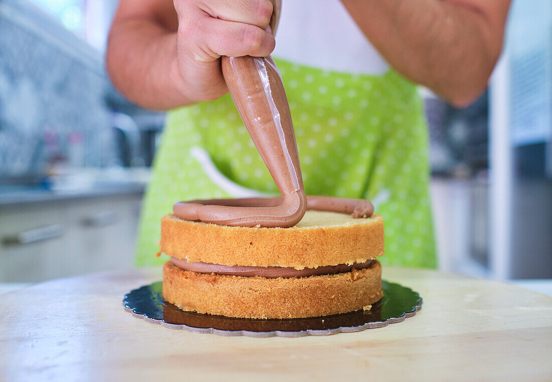 Bäckerin gibt Schokoladencreme aus Spritzbeutel auf Biskuitkuchen